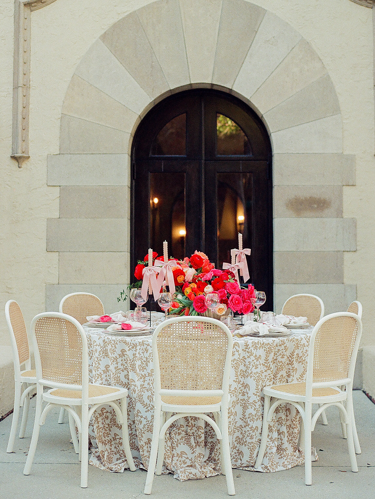 A wedding reception table with many pink flowers and white chairs sits on a patio at the Powel Crosley Estate Wedding venue