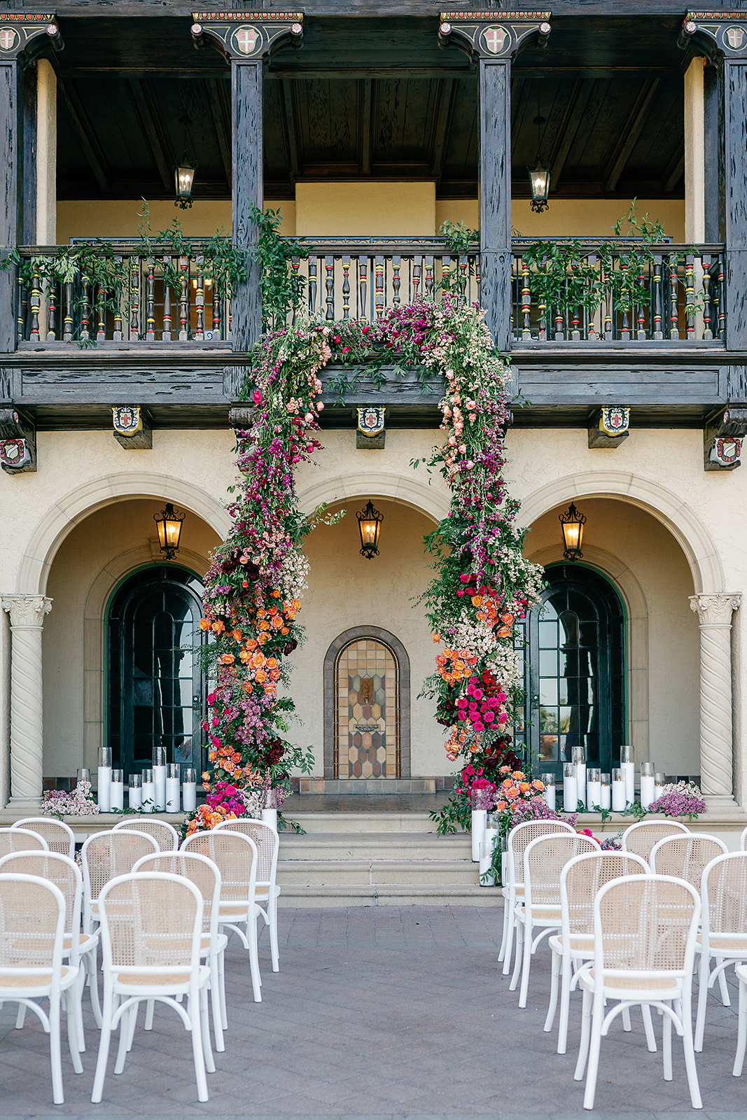 Details of a Powel Crosley Estate Wedding ceremony set up with a large colorful floral arch and white wicket chairs