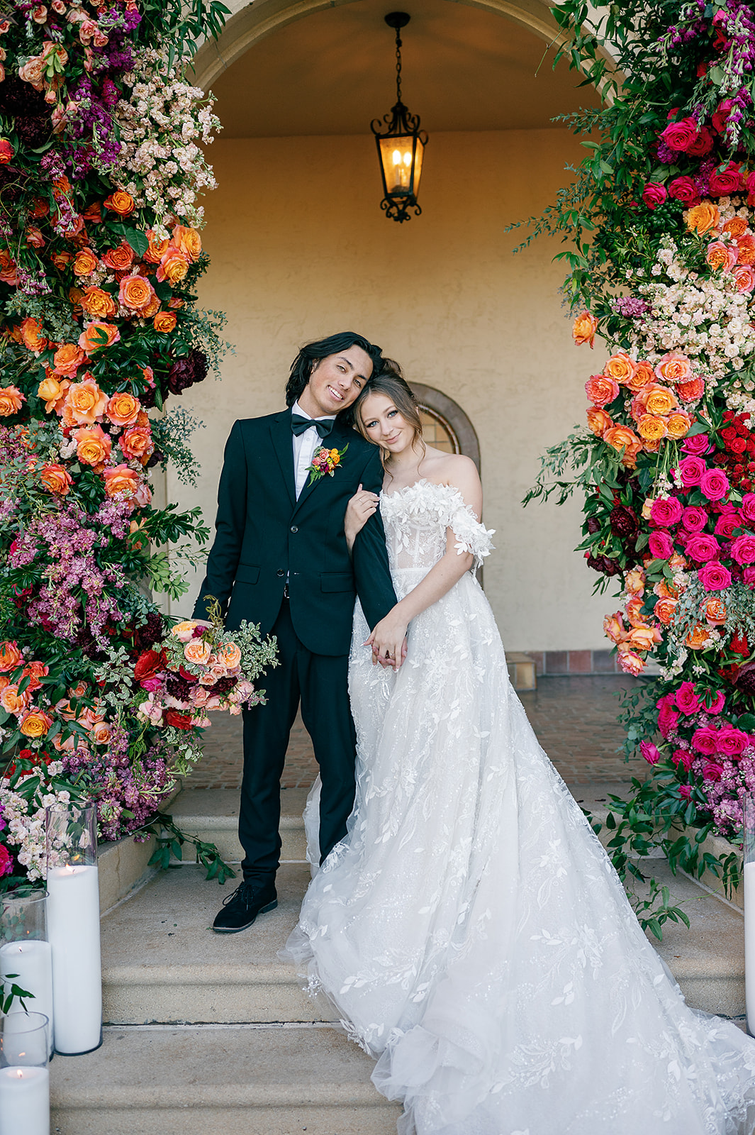 Newlyweds hug and smile while standing under a colorful floral arch