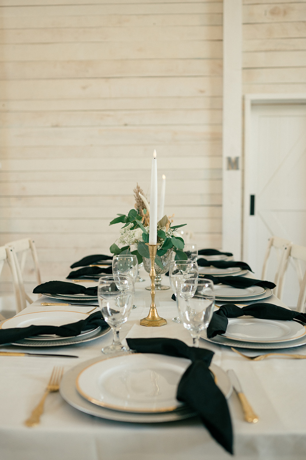 A wedding reception table set up with candles and black napkins on white linen at The White Dove Barn wedding venue