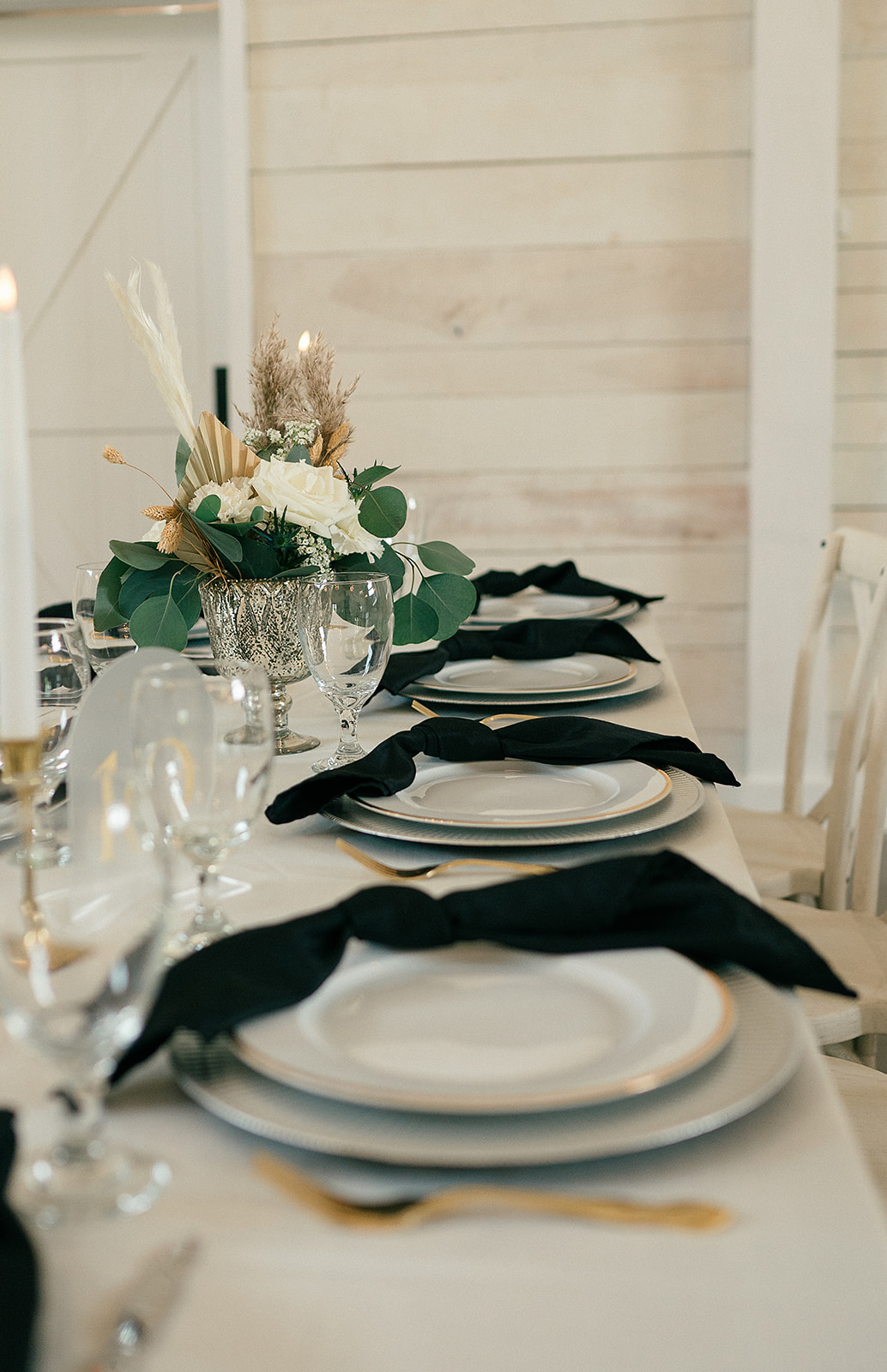 A view of details of a table setting with gold silverware and black napkins at The White Dove Barn